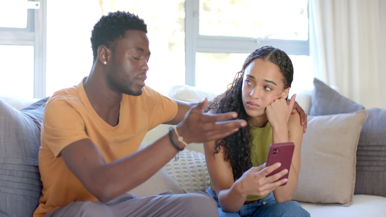 Casal Afro-Americano no Sofá em Casa, Mulher Lendo Mensagem no Telefone, Homem se Inclinando para Confortar