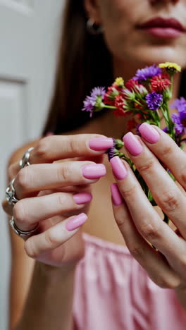 woman's hands with pink nails and rings holding a colorful flower bouquet