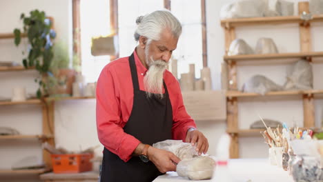 un alfarero biracial feliz con larga barba trabajando y sonriendo en un estudio de cerámica, en cámara lenta