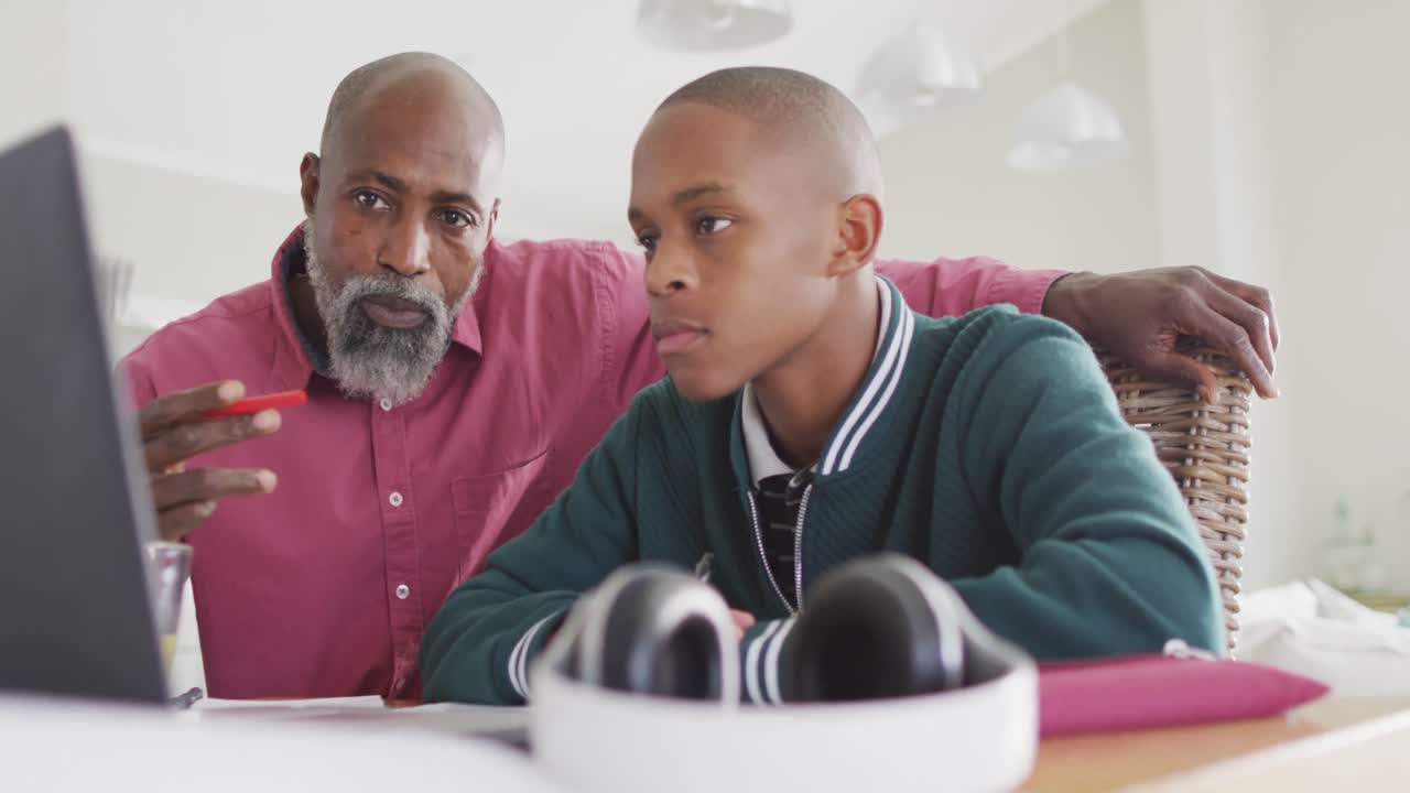 Video of happy african american father and son doing homework together