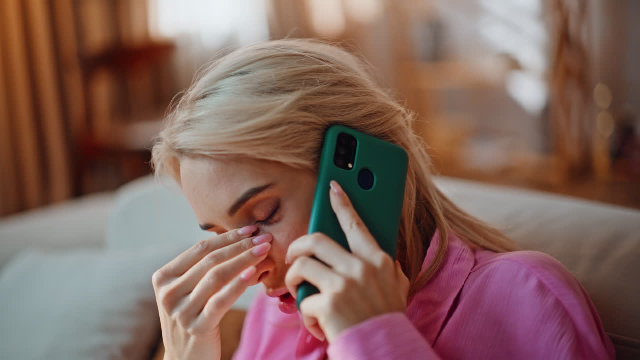 Upset woman smartphone call in living room portrait. Blonde girl having migraine