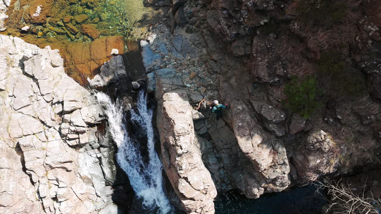 Top down aerial shot of hiker climbing rocky trail near small waterfall, Italy