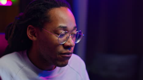 a young man in a pink shirt with dreadlocks and glasses looking at the camera