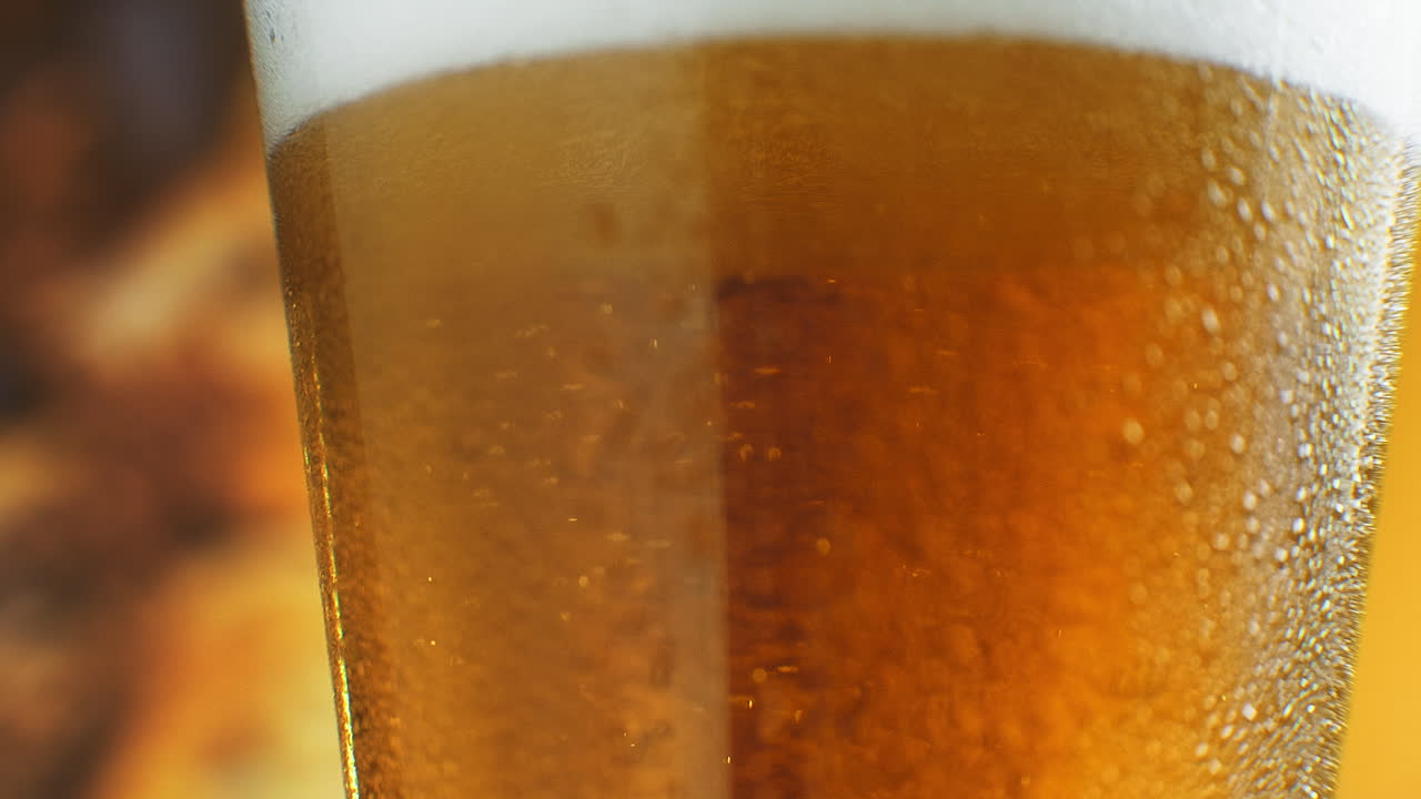 Birra che si versa in un bicchiere inclinato. IPA alla spina. Birra chiara fredda in un bicchiere con goccioline d'acqua. Birra artigianale che forma onde in primo piano. Freschezza e schiuma. Sfondo di bar. Birra artigianale di microbirrificio
