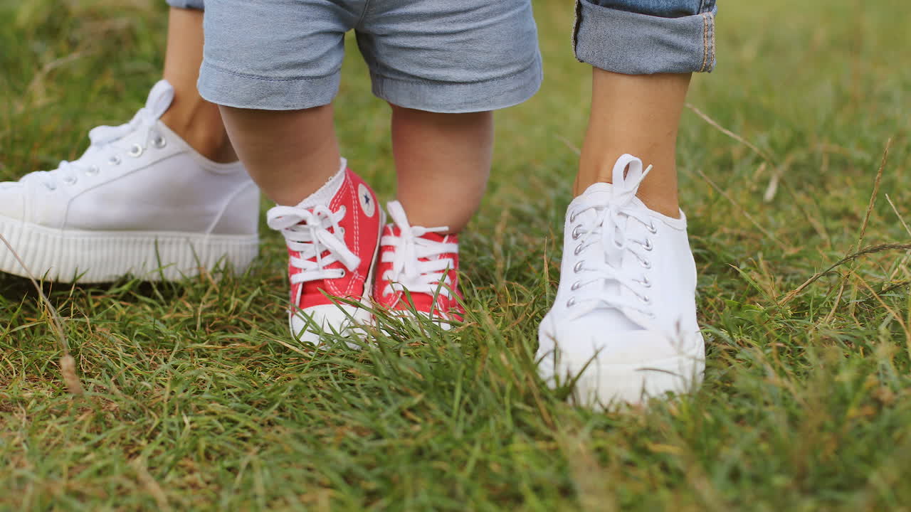 운동화를 신고 푸른 잔디에서 첫 발을 내딛는 어머니와 함께 알아볼 수 없는 어린 소년을 닫습니다