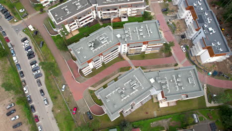 top down aerial - flying over a residential building complex situated near trees and nature - view of the roof and technical installation