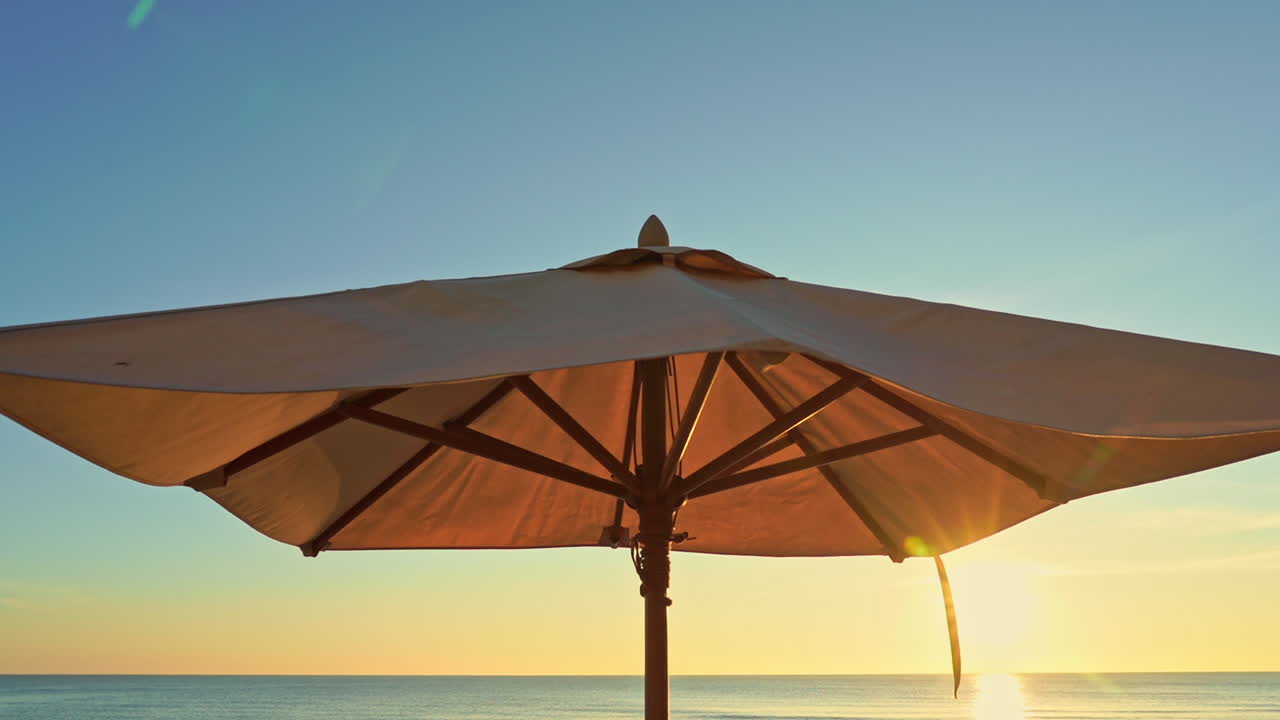 Brown sun umbrella against clear sky on sunset, sea water on horizon, close up