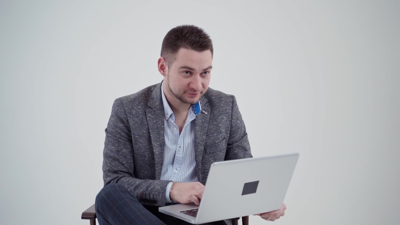 Businessman working on a laptop. Man in stylish costume looking into the laptop and becomes happy on white background. Slow motion.