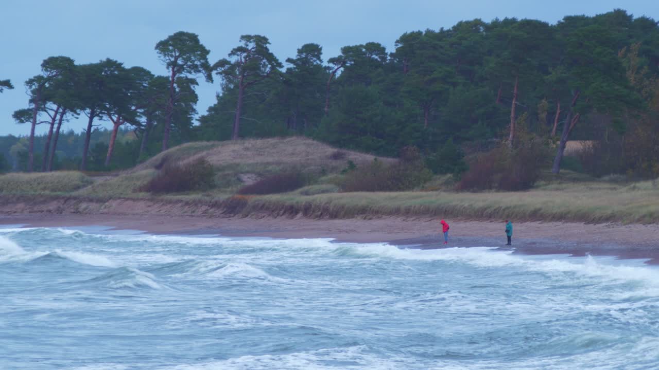 흐린 가을 날 리파자(liepaja)의 모래 카로스타 해변에 부서지는 파도, 먼 거리의 사람들이 걷고, 멀리서 총격을 가합니다.