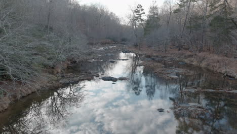 cielo reflejado en el río en un ominoso paisaje forestal sin hojas, aéreo