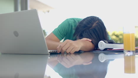 Teenage-Asian-boy-rests-his-head-on-a-desk-at-home-while-studying