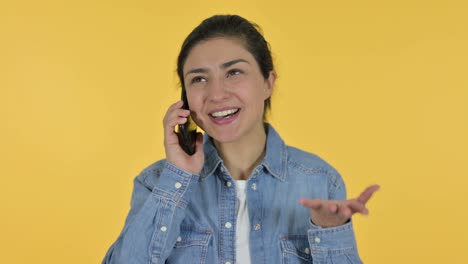 young indian woman talking on smartphone, yellow background