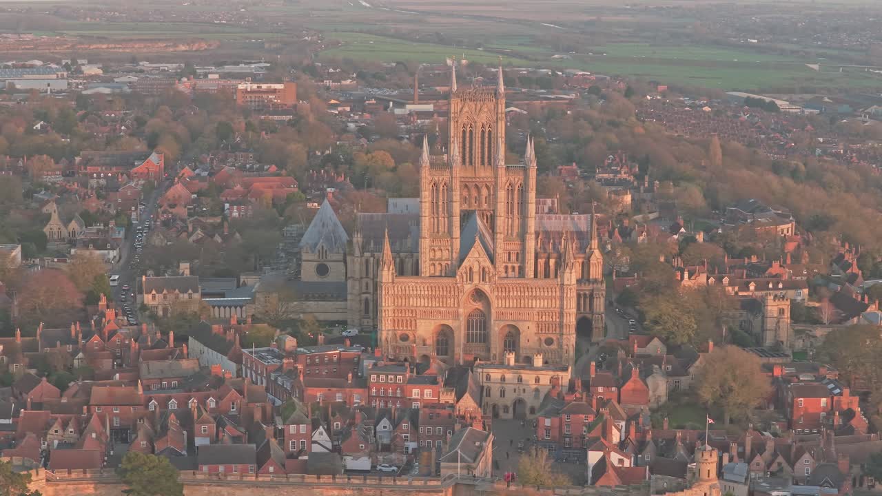 Lincoln Cathedral Church of the Blessed Virgin Mary of Lincoln illuminated by warm sunrise light as rises historic rooftops and scape revealing gothic architectural details, Drone establishing shot