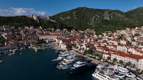 Parallax drone shot of Hvar harbor during the day with Adriatic Sea, boats and castle in Croatia