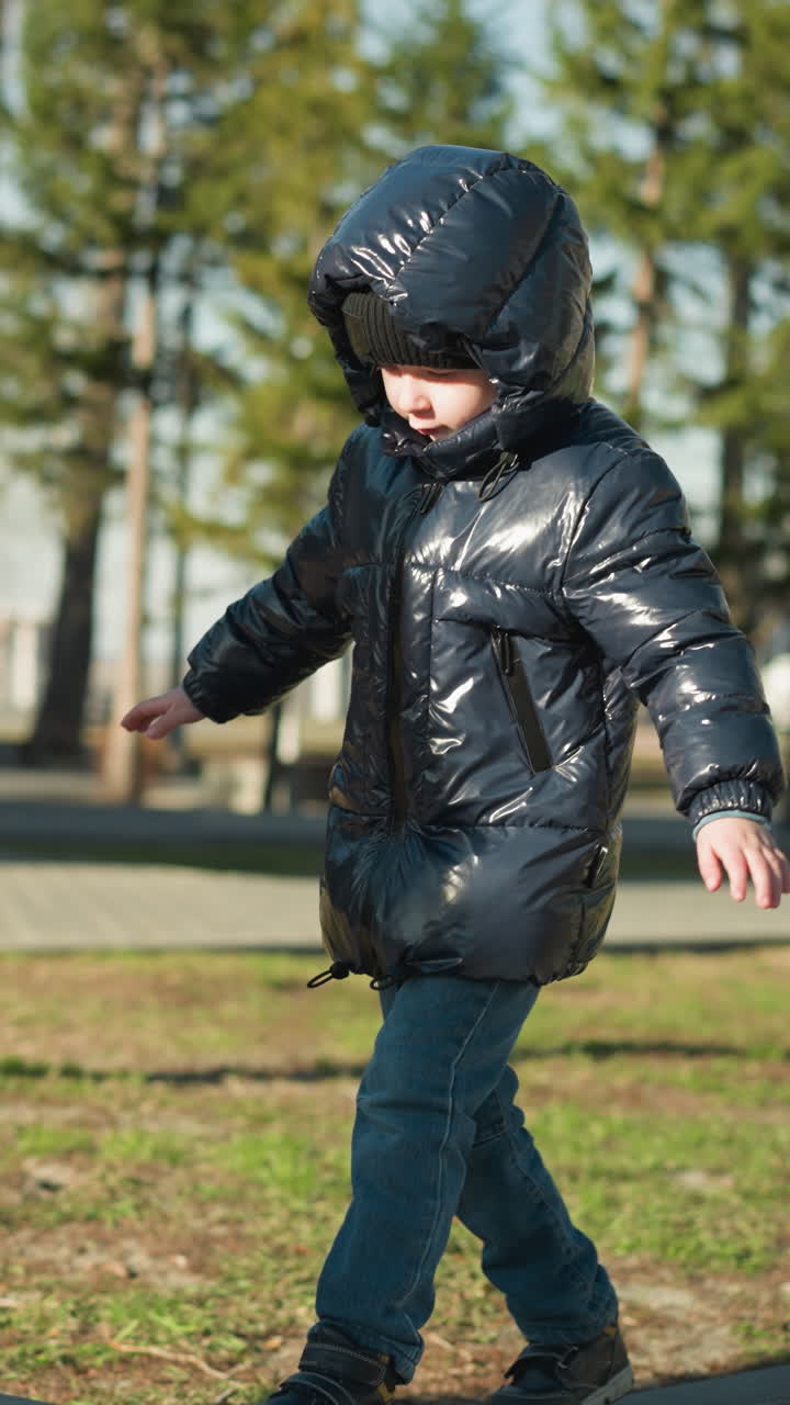 나무와 근처 건물의 배경으로 반이는 검은색 재을 입고 균형을 위해 팔을 펴고 보행로를 조심스럽게 고 있는 어린 아이의 클로즈업