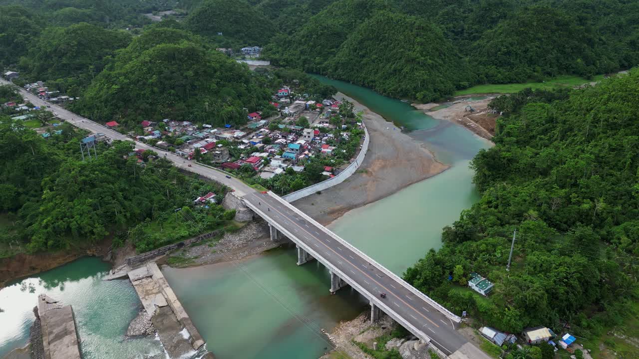 Panoramic drone flyover shot of lush mountainside village community along Sto Domingo River and Bridge at Catanduanes, Philippines