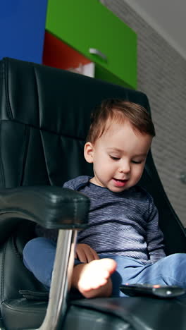 beautiful toddler swinging in the big leather chair. child plays with tv remote and saying something. low angle view. vertical video