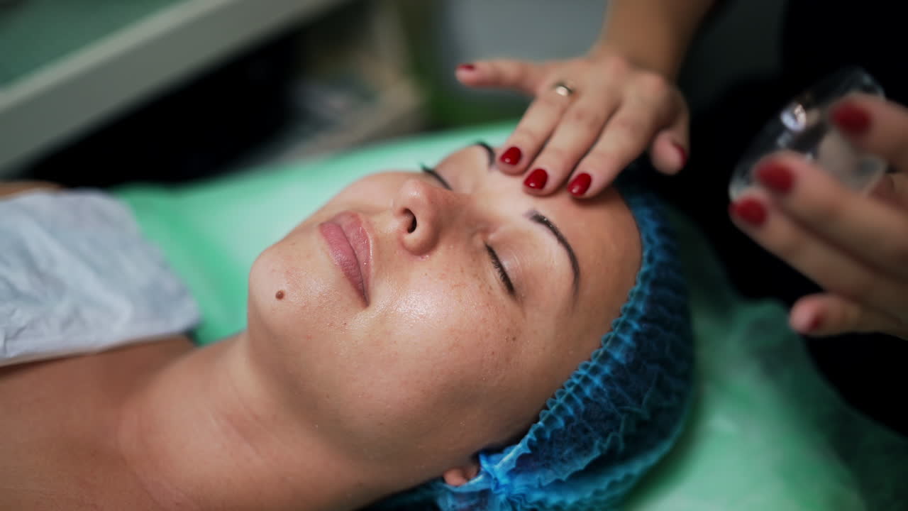 Bare hands of cosmetologist cover woman's face with transparent gel. Beauty and skincare concept. Salon procedures. Close up.