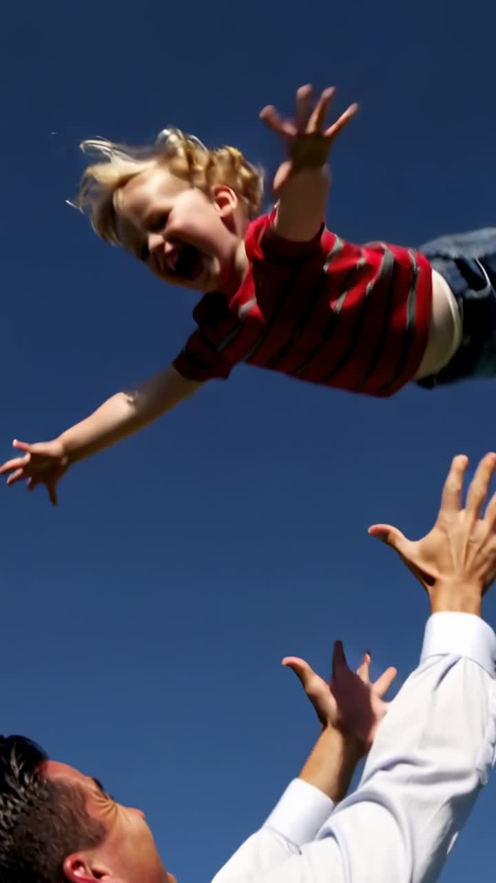 Vertical video: Smiling father lifting toddler, tossing and catching to hug in field with tie