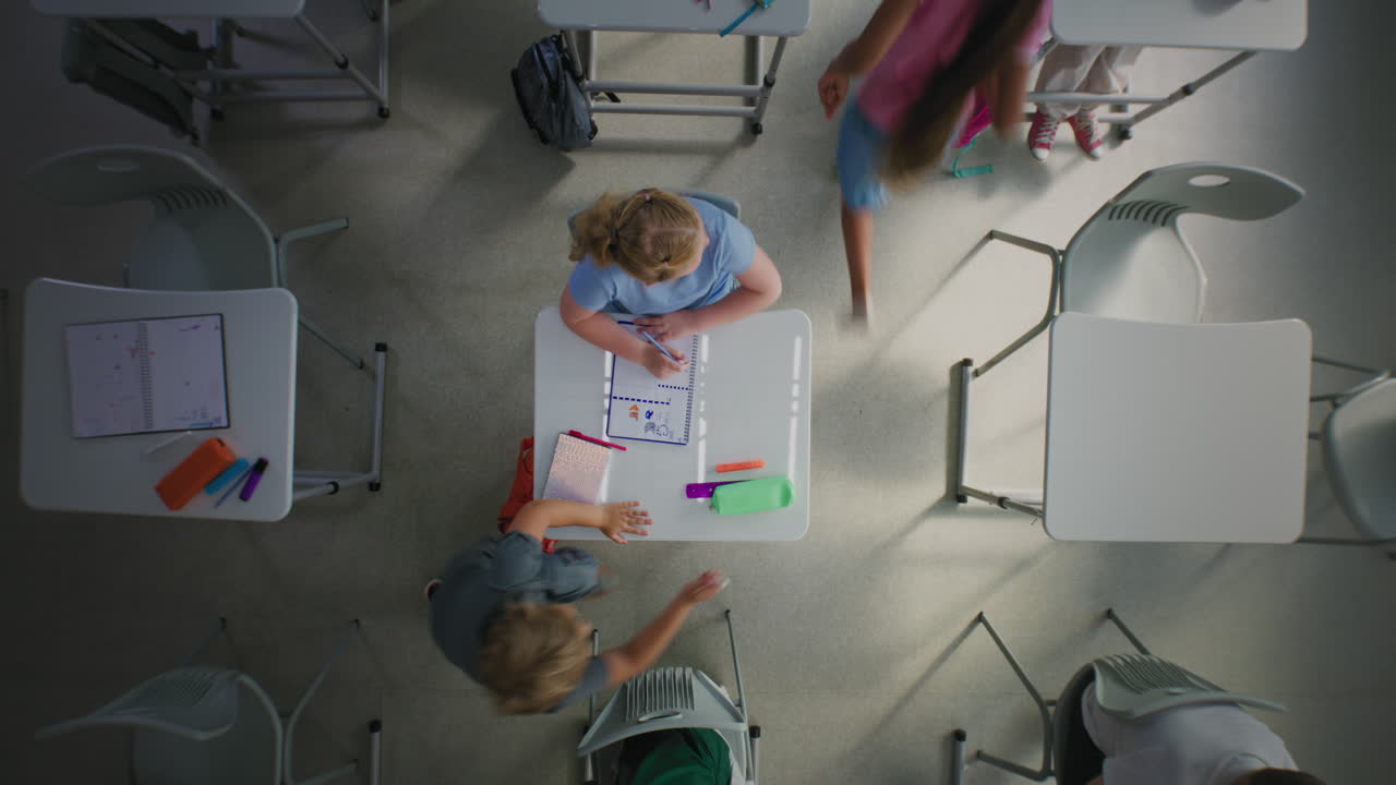 Rotating Top View on Elementary School Girl Drawing in School Notebook in Classroom