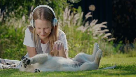 teenage girl plays with a puppy, lies on the lawn, listens to music on headphones