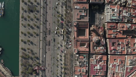 Vehicles-driving-on-multilane-road-along-waterfront-at-Port-Vell.-Top-down-panning-view-of-buildings-and-traffic-in-city.-Barcelona,-Spain