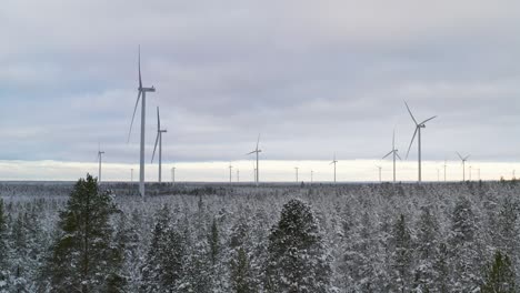 Dolly-in-shot-of-a-wind-farm-during-winter-in-the-middle-of-forest-full-of-snow,-wind-energy-concept