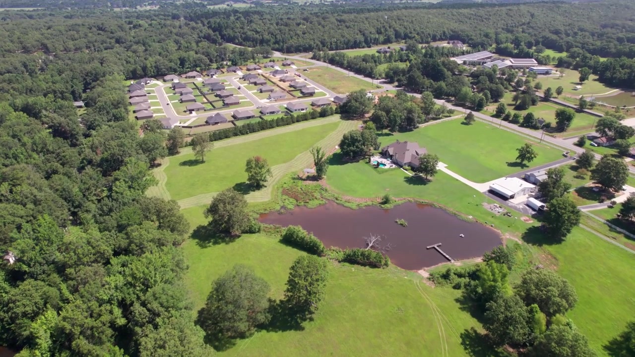 Aerial video of some fields and houses in Wooster Arkansas. Camera flies over a pond.