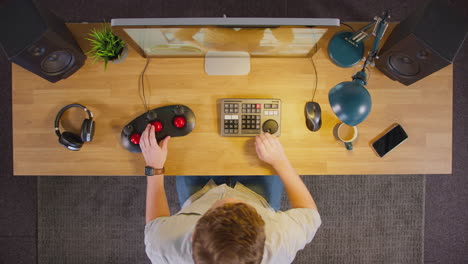 overhead view of male video editor with coffee working at computer screen in office at night