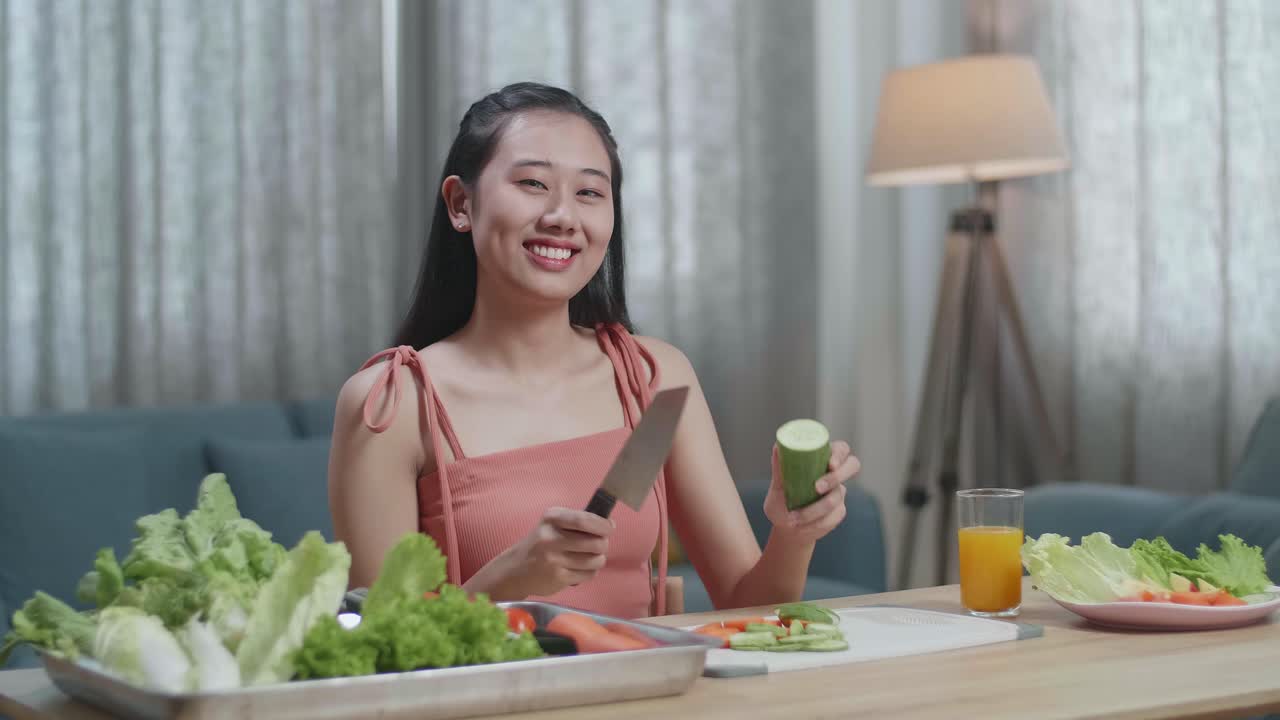 집에서 카메라에 포즈를 취하기 전에 칼을 들고 호박을 잘라내는 미소 짓는 아시아 여성