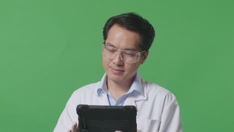 close up of smiling asian man scientist working on a tablet while standing on the green screen background in the laboratory