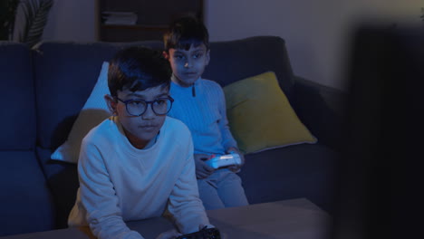 two young boys at home fighting over controllers playing on computer games console on tv late at night 2