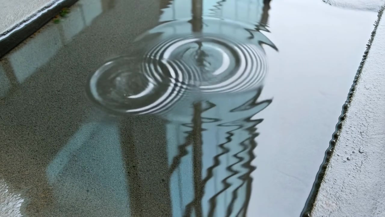 Close low-angle view of concentric circular ripples propagating across shallow rectangular water channel next to granular concrete ledge