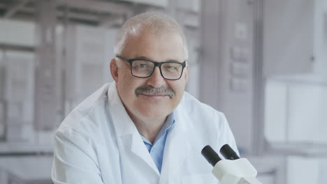 retrato de un médico masculino en un laboratorio con un microscopio mirando a la cámara serio. médico el médico sonríe a la cámara. imágenes de alta calidad 4k