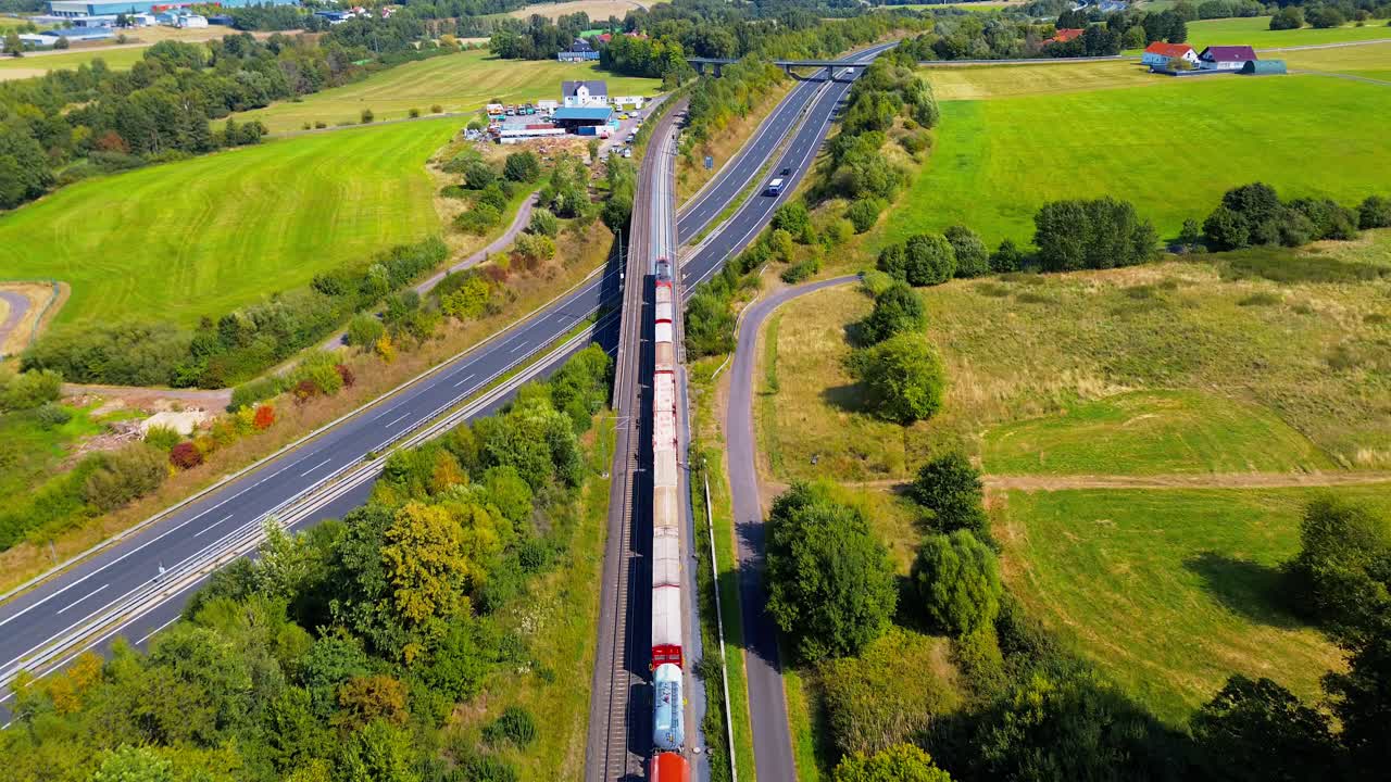 Freight Train Traveling Beside Busy Highway Through Countryside Captured from Aerial Drone
