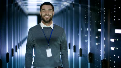 un ingeniero de servidores masculino trabajando en una computadora portátil en un centro de datos, cierra el cuaderno y sonríe.