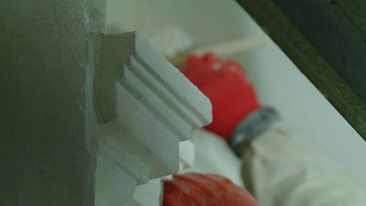 Shot of a construction worker painting white architectural trim molding on a wall using a paintbrush during an indoor renovation or repair project