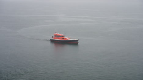 Small-Orange-Pilot-Boat-In-Ocean-On-Rainy-Day,-Slow-Motion-4K-Drone