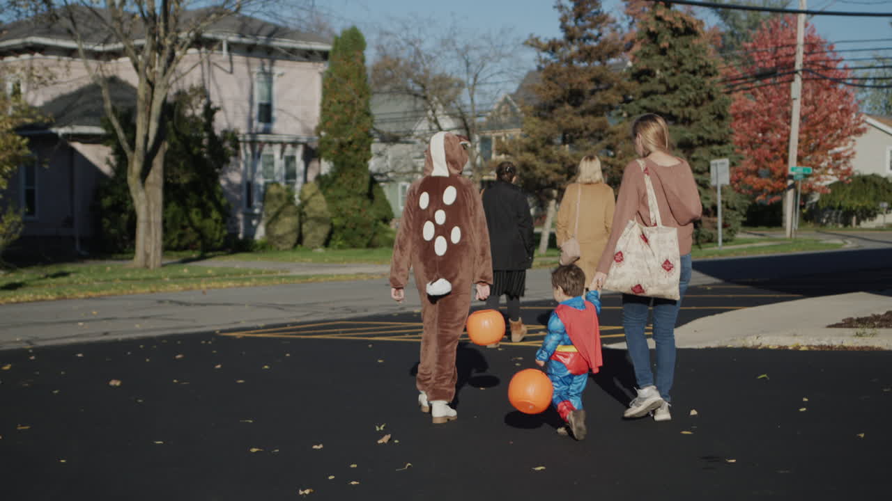 una familia con niños camina por la calle de una típica ciudad estadounidense. los niños están vestidos con trajes de halloween. van a recoger dulces