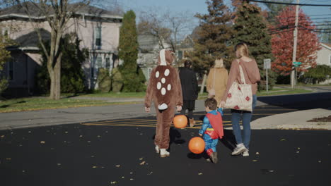 a family with children walks along the street of a typical american town. the children are dressed in halloween costumes. going to collect candy