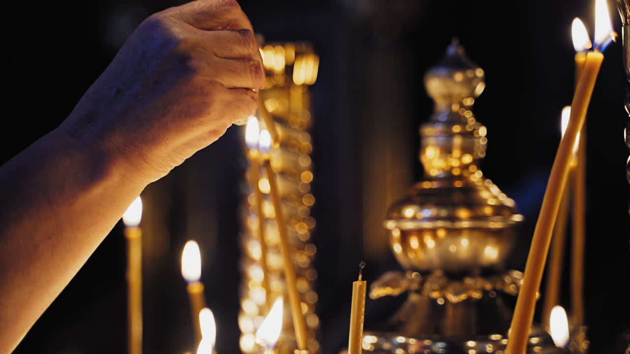 Female's hand is lighting a yellow candle in church. Burning candles in the night temple during worship. People put glowing candles for prayer intentions.
