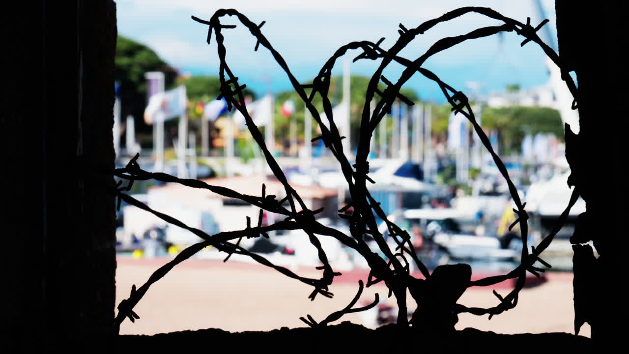 Close up of barbed wire loops with a blurred view of boats docked in a harbour in daylight