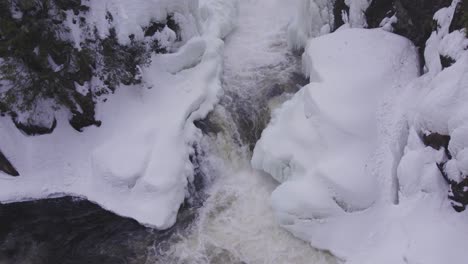 aerial drone shot of a frozen waterfall nestled in a wintry forest landscape