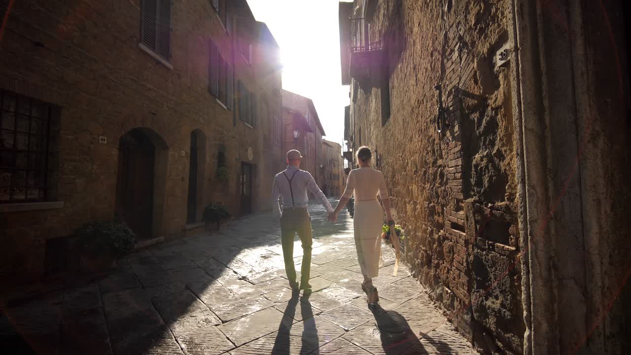 Retro-par går i rustikk gate i Toscana mens de holder hender ved soloppgang