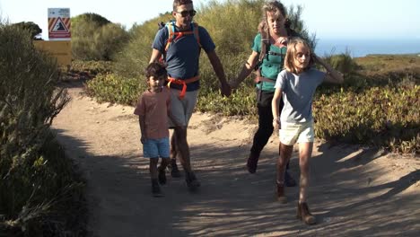 Kids-and-parents-wearing-backpacks-walking-on-path-in-mountains