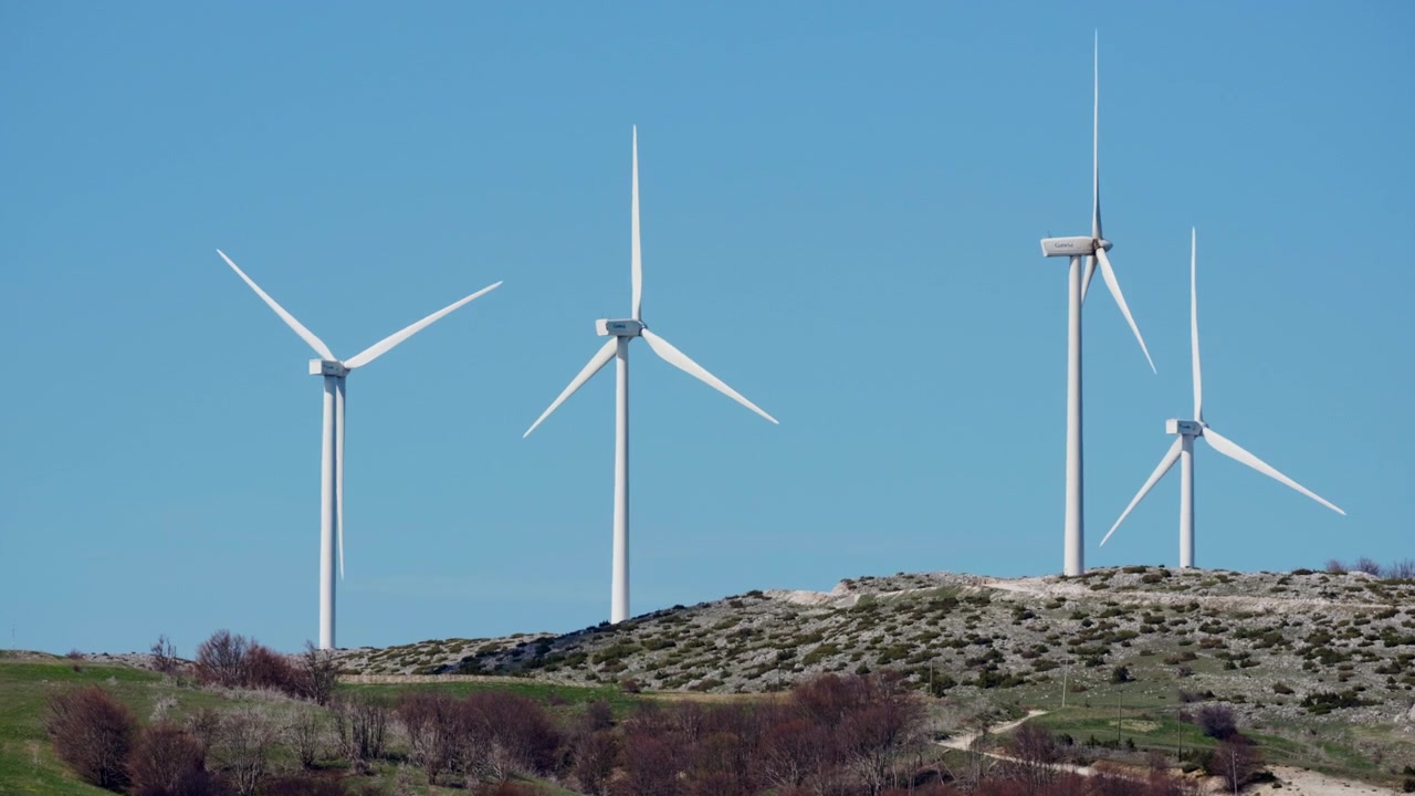 Le turbine eoliche girano costantemente sulla cima di una collina rocciosa contro un cielo azzurro limpido. Ideale per discussioni sull'energia rinnovabile e la sostenibilità ambientale.