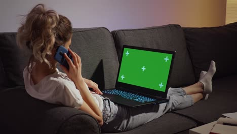 mujer hablando por teléfono y trabajando en la pantalla verde de la computadora portátil.