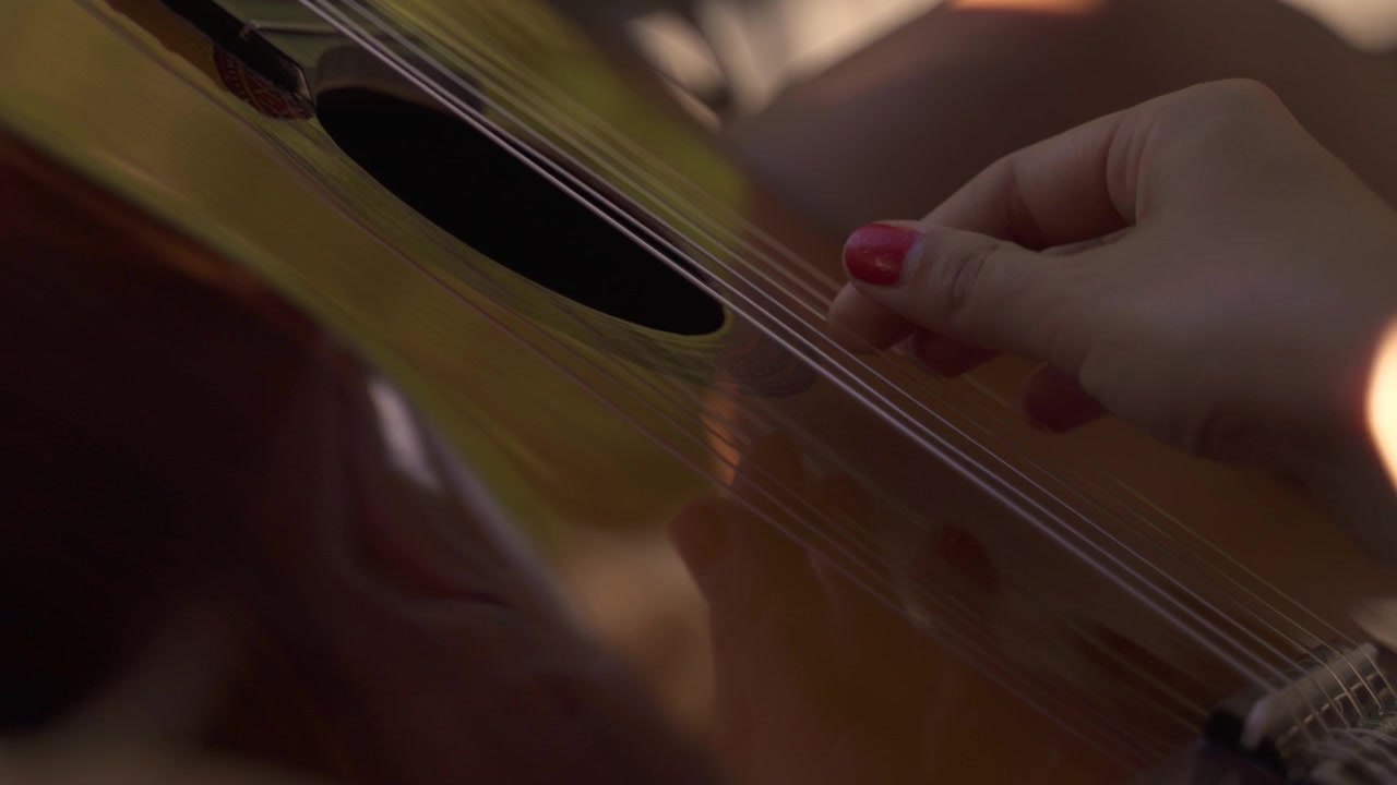 4K Jovem mulher tocando violão gentilmente ao ar livre à luz do dia, close-up 2.