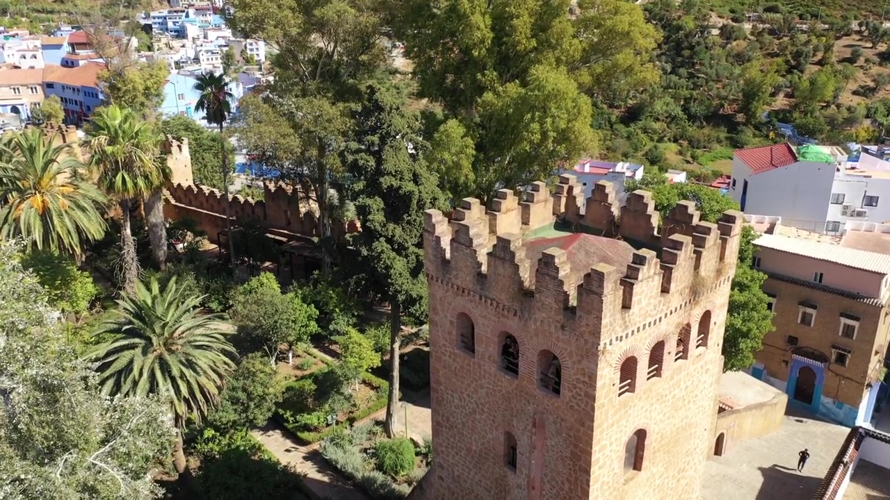 Widok z lotu ptaka z drona na historyczną Kasbę Chefchaouen, prezentujący jej ikoniczną kamienną wieżę, ogrody andaluzyjskie i dziedzictwo kulturowe w sercu słynnego Niebieskiego Miasta Maroka