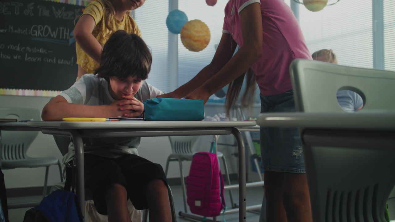 Depressed Primary School Boy Sitting at Desk While Aggressive Classmates Abusing Him